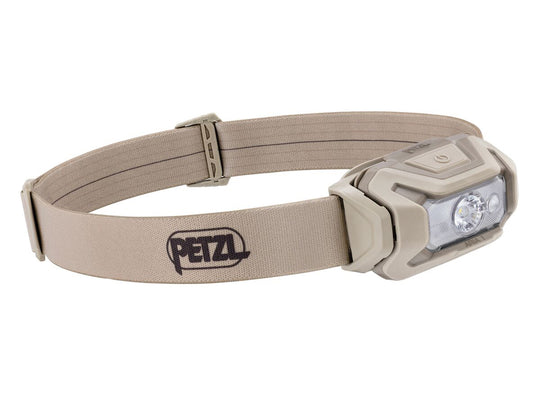 A Petzl headlamp with a beige adjustable elastic strap and a matching beige housing, featuring a clear lens and visible LED light elements, on a plain white background.